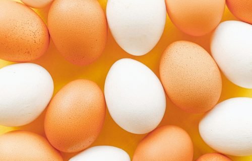 Top view of brown and white eggs arranged on a vibrant yellow surface, offering a minimalistic food pattern.