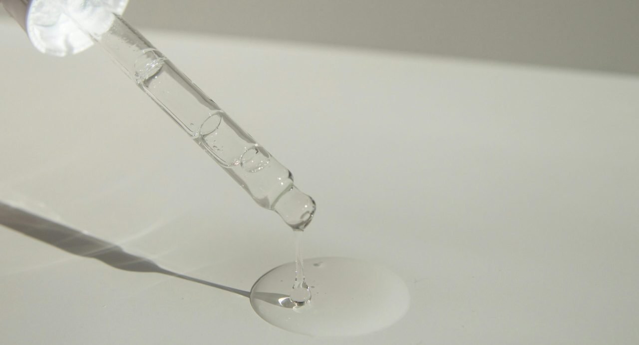 Close-up of a cosmetic pipette releasing serum onto a surface with soft sunlight.