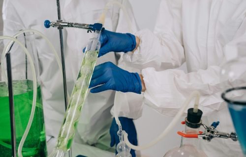 Researchers in protective gear conducting a chemistry experiment with laboratory apparatus.